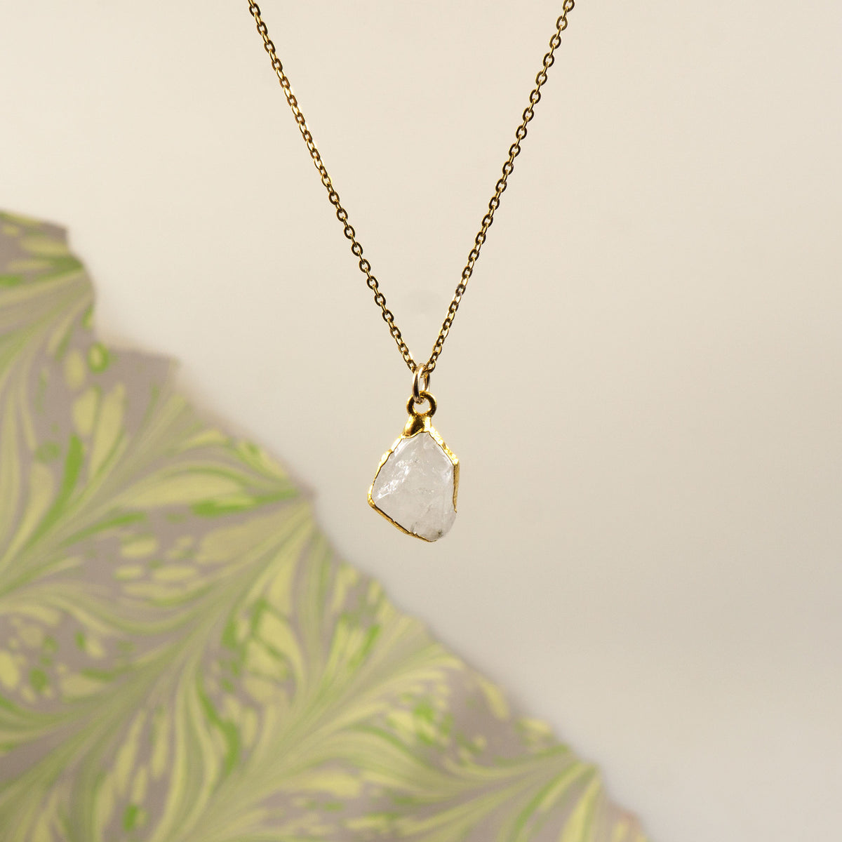 A delicate gold chain necklace with a raw, irregular-cut white Rainbow Moonstone stone pendant.
