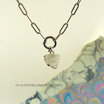 A silver paperclip chain necklace with a small triangular clear Rainbow Moonstone pendant