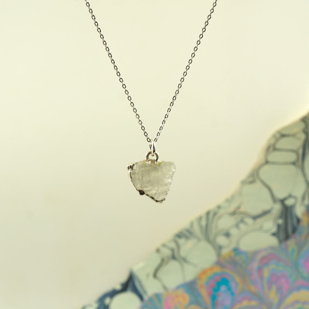 A silver chain necklace with a raw, irregular-cut Rainbow Moonstone pendant.