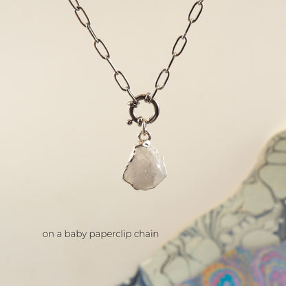 A silver paperclip chain necklace with a large ring connector and a raw, faceted clear Rainbow Moonstone gemstone pendant.