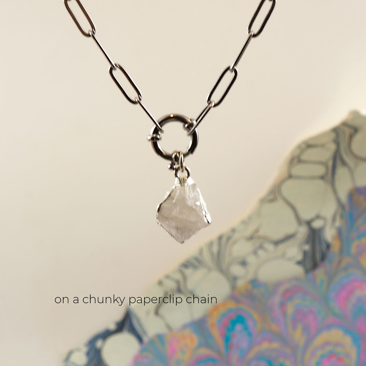 A silver paperclip chain necklace with a large ring connector and a raw, faceted clear Rainbow Moonstone crystal pendant.