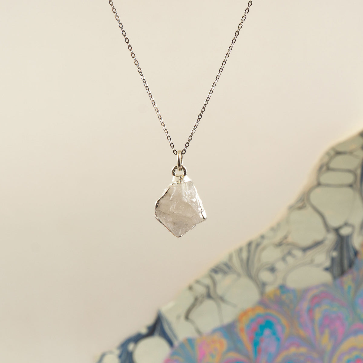 A silver chain necklace with a raw, irregular faceted Rainbow Moonstone crystal pendant
