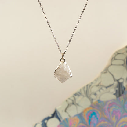 A silver chain necklace with a raw, irregular faceted Rainbow Moonstone crystal pendant
