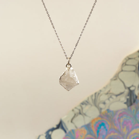A silver chain necklace with a raw, irregular faceted Rainbow Moonstone crystal pendant