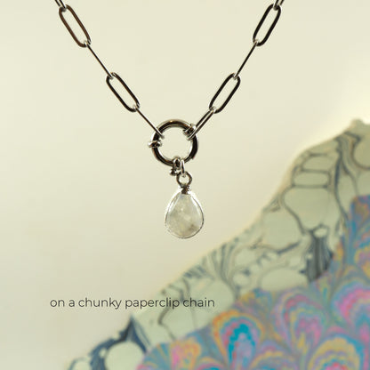 A silver paperclip chain necklace with a circular ring clasp holding a clear teardrop Rainbow Moonstone pendant.