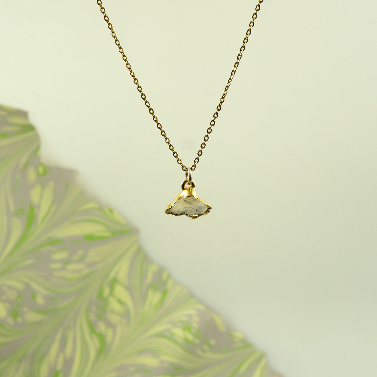 A gold chain necklace with a small pendant made from a natural, polished white Rainbow Moonstone.