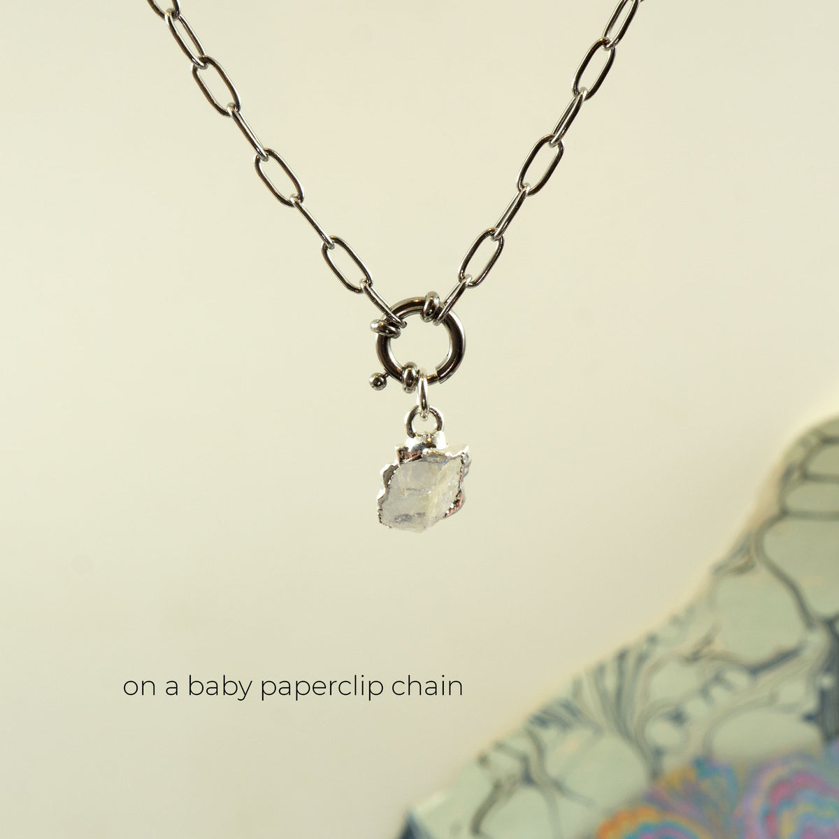 A silver paperclip chain necklace with a small ring clasp and a clear faceted Rainbow Moonstone gemstone pendant,