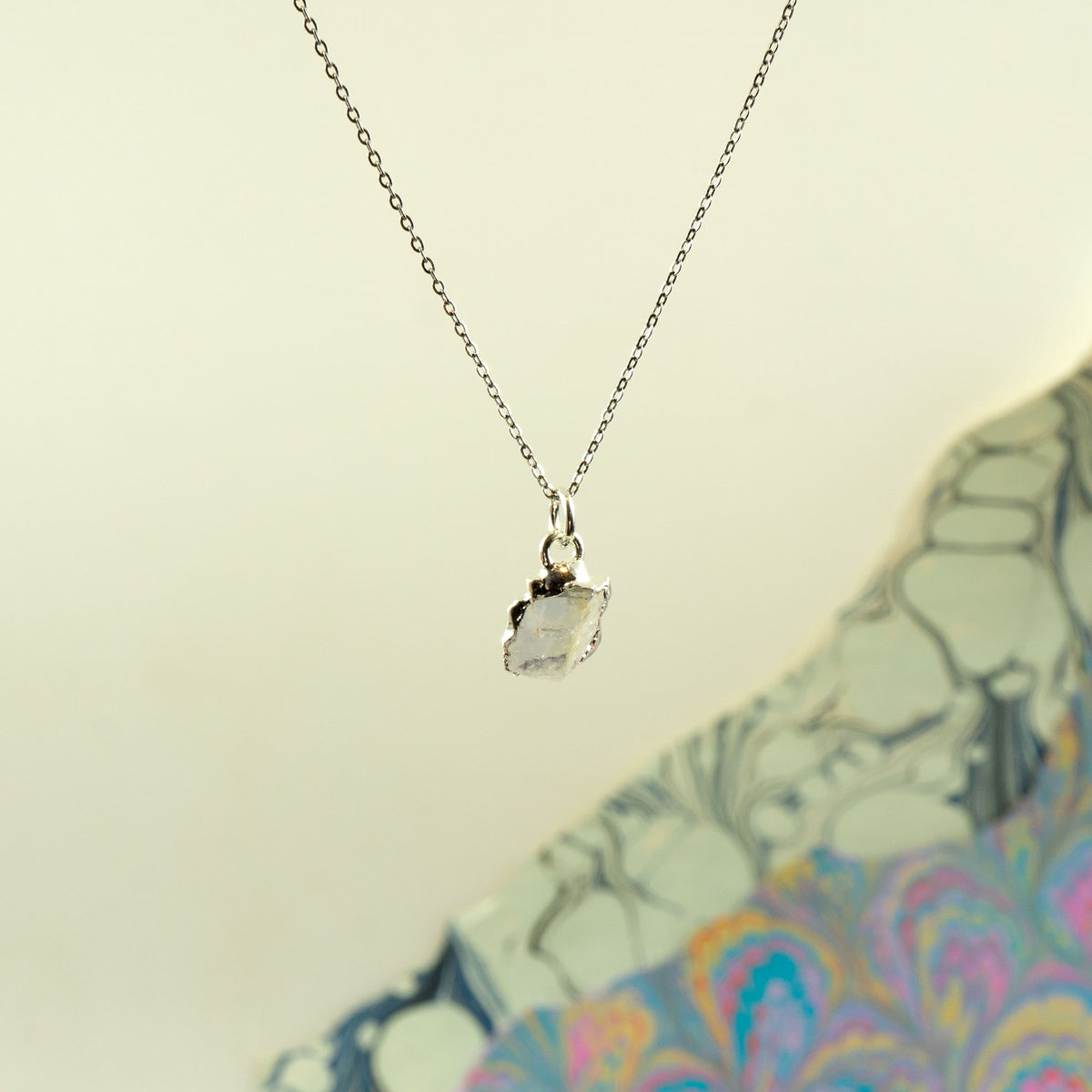 A delicate silver chain necklace with a raw, irregular-cut clear Rainbow Moonstone pendant