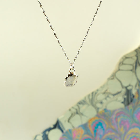 A delicate silver chain necklace with a raw, irregular-cut clear Rainbow Moonstone pendant