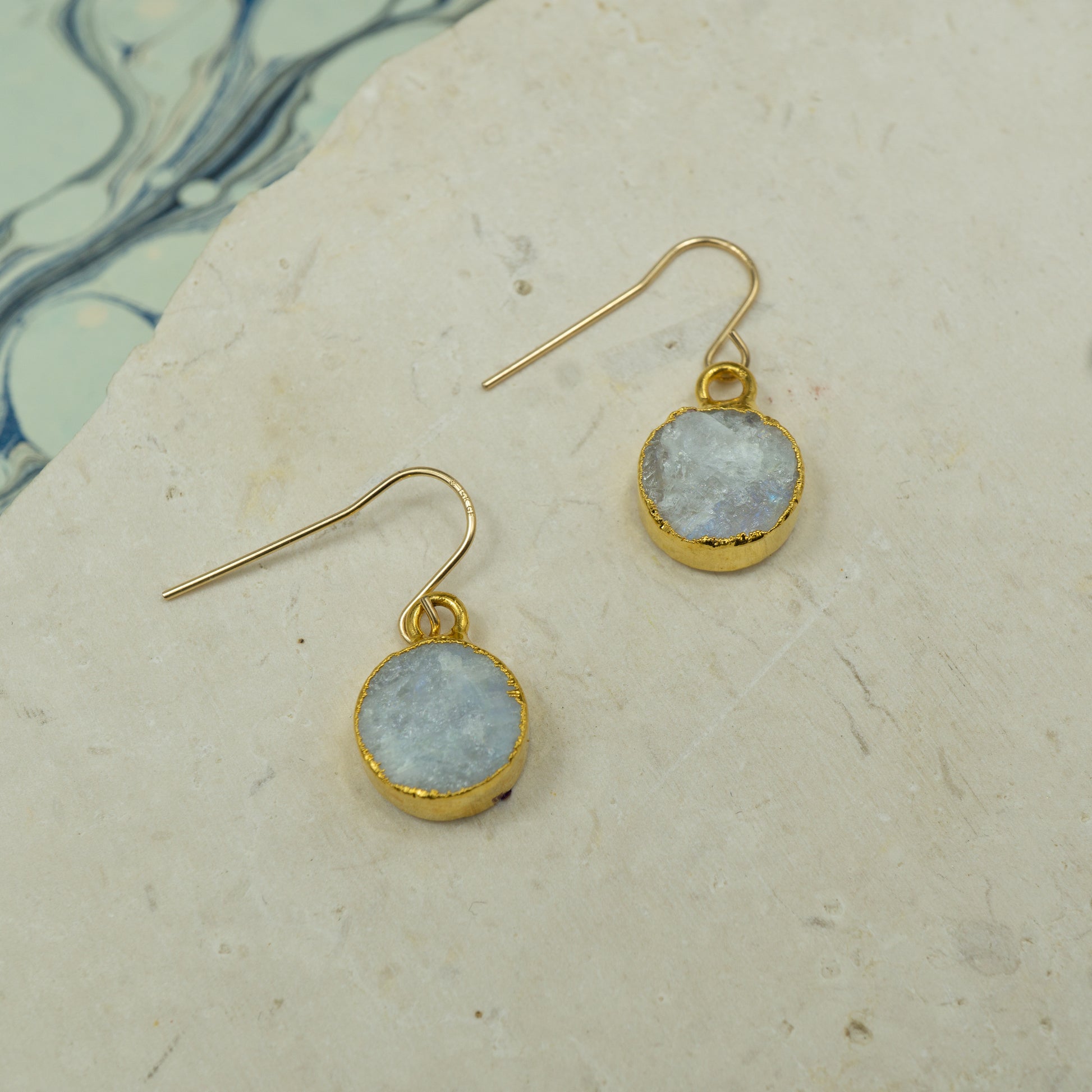 Round raw white moonstone earrings on hooks finished in gold.
