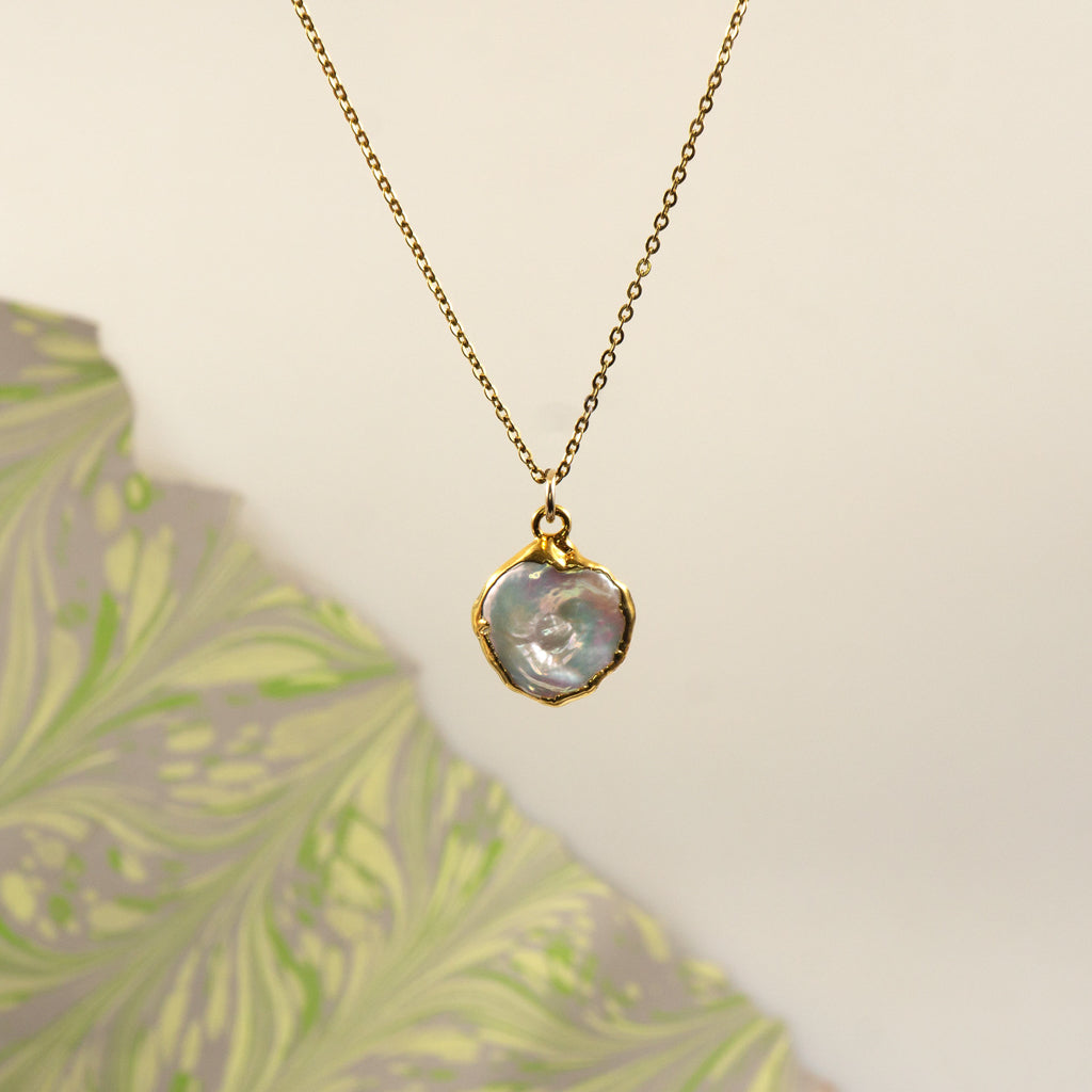 A gold chain necklace with a round, irregular  pearl pendant