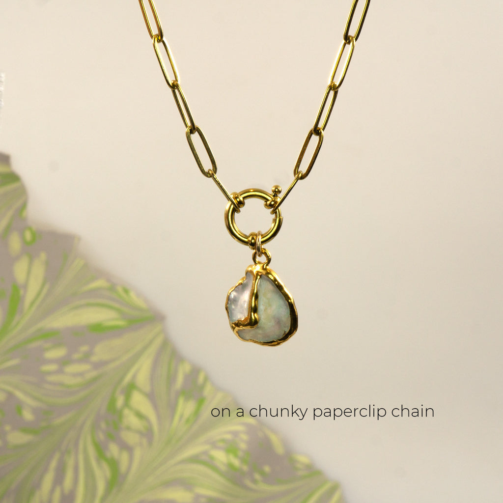 A gold paperclip chain necklace with a gold ring clasp a irregular iridescent pearl pendant