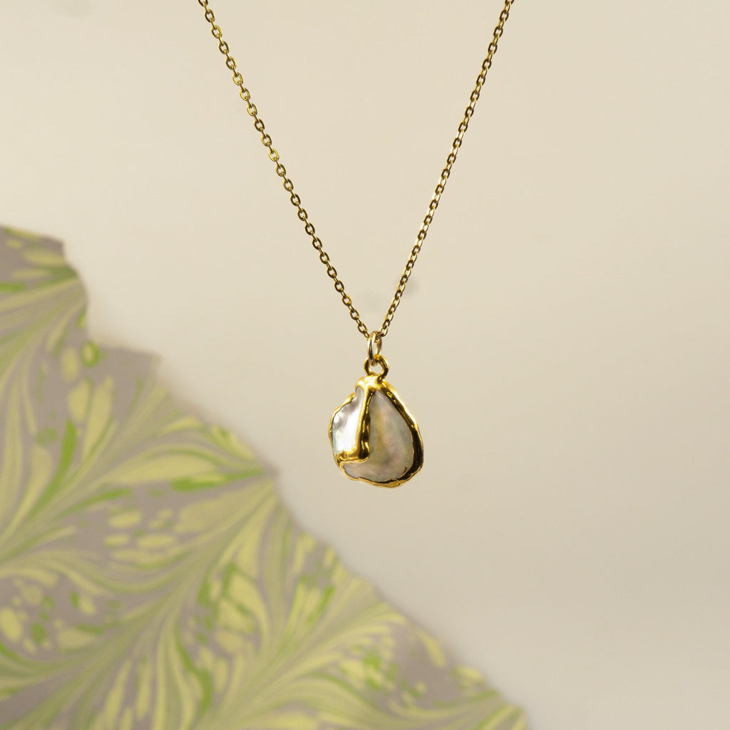 A gold chain necklace with an organic, irregularly shaped pendant made from a polished pearl pendant