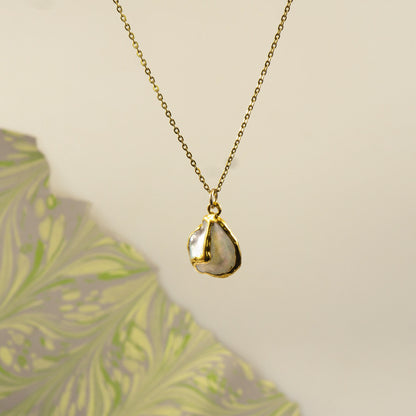 A gold chain necklace with an organic, irregularly shaped pendant made from a polished pearl pendant