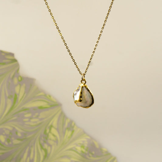A gold chain necklace with an organic, irregularly shaped pendant made from a polished pearl pendant