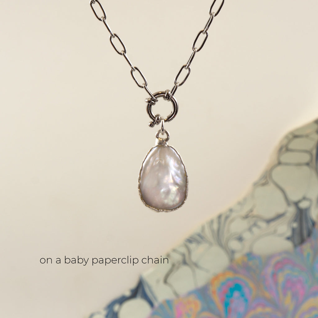 A silver pendant necklace featuring a teardrop-shaped iridescent pearl on a silver paperclip chain