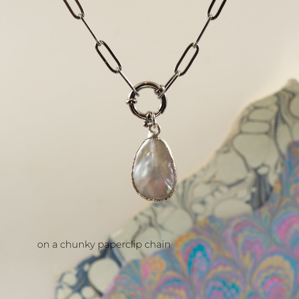 A silver paperclip chain necklace with a circular ring connector holding a teardrop-shaped iridescent pearl pendant,