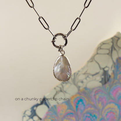 A silver paperclip chain necklace with a circular ring connector holding a teardrop-shaped iridescent pearl pendant,
