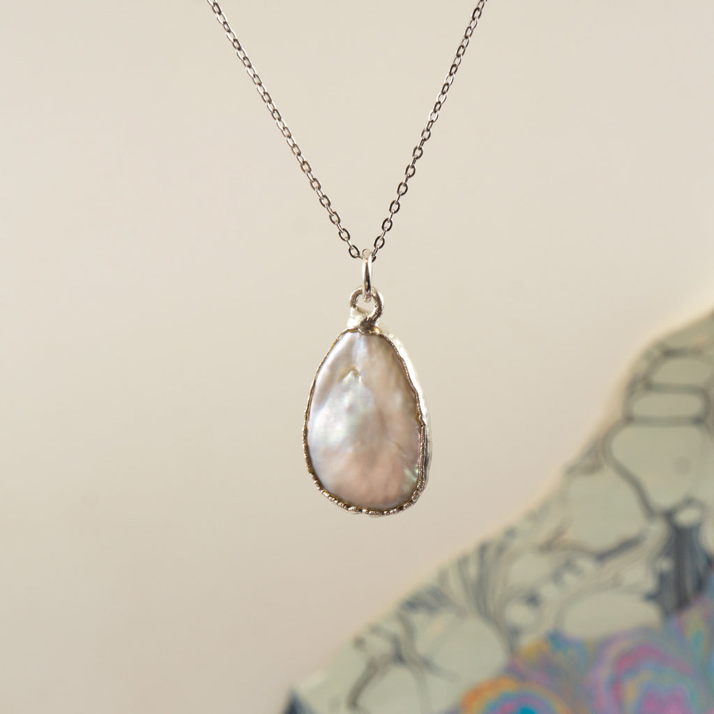 A silver chain necklace with a teardrop-shaped pendant made of iridescent pearl, 