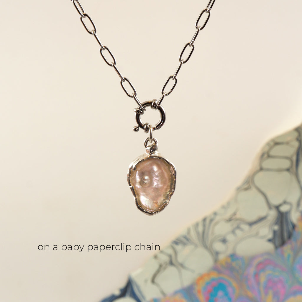 A silver paperclip chain necklace with a small ring clasp holding an irregular, pearl pendant, 