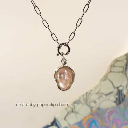 A silver paperclip chain necklace with a small ring clasp holding an irregular, pearl pendant, 