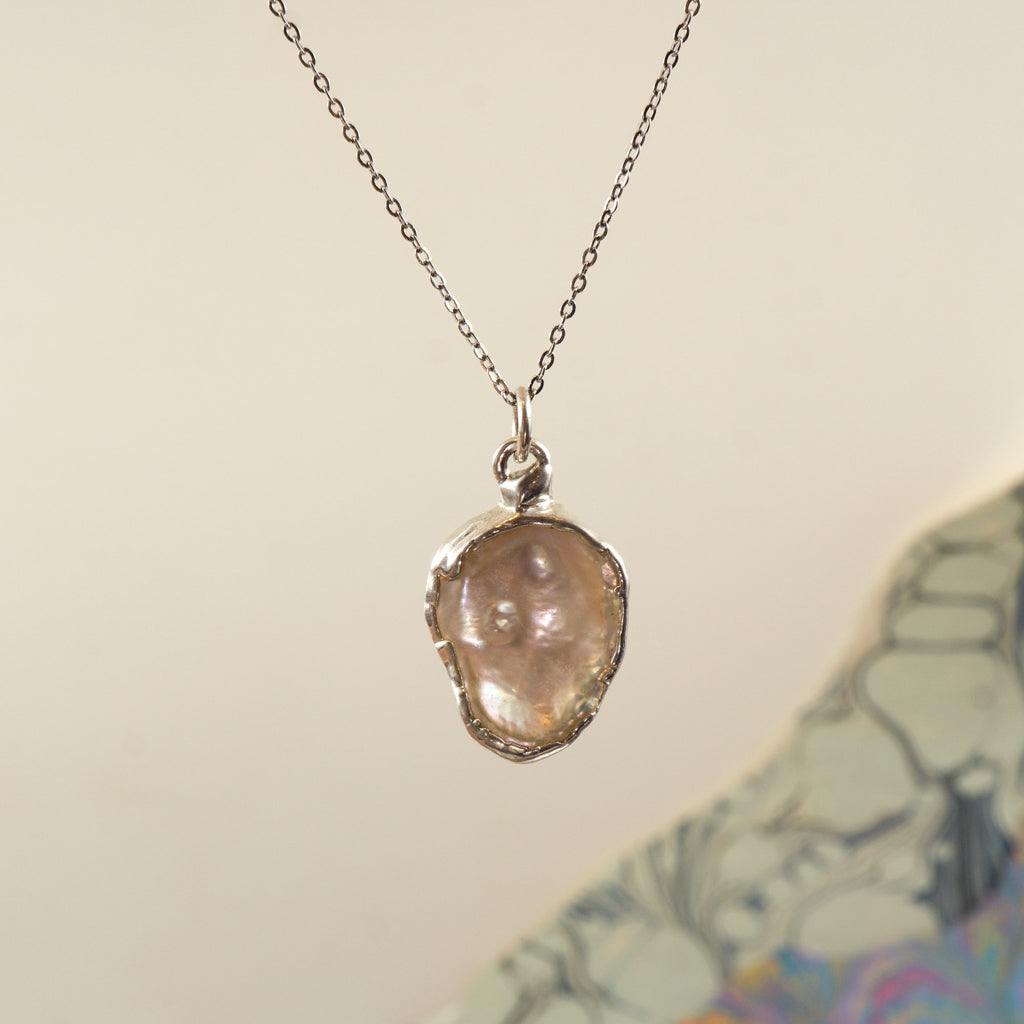 A silver chain necklace with an irregular, pearl pendant in a silver