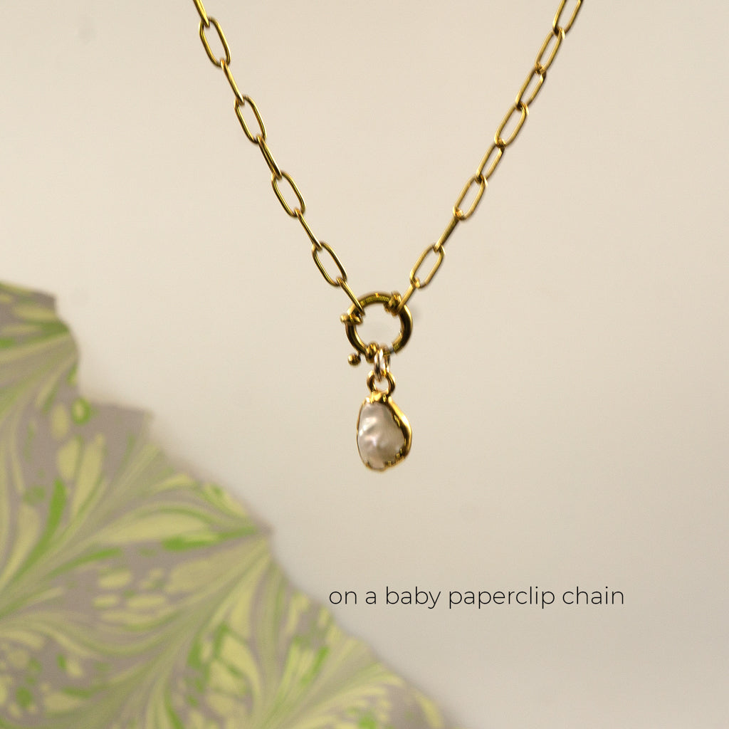 A gold paperclip chain necklace with a small gold clasp holding a irregular shaped white pearl pendant