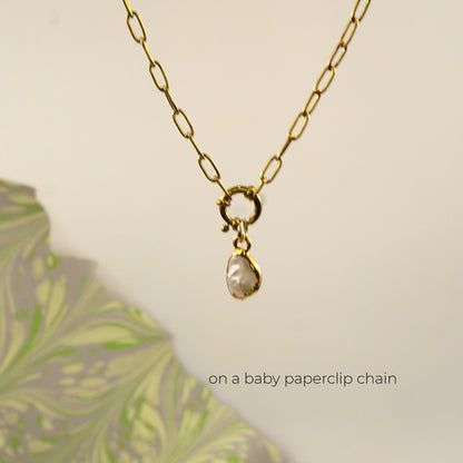 A gold paperclip chain necklace with a small gold clasp holding a irregular shaped white pearl pendant
