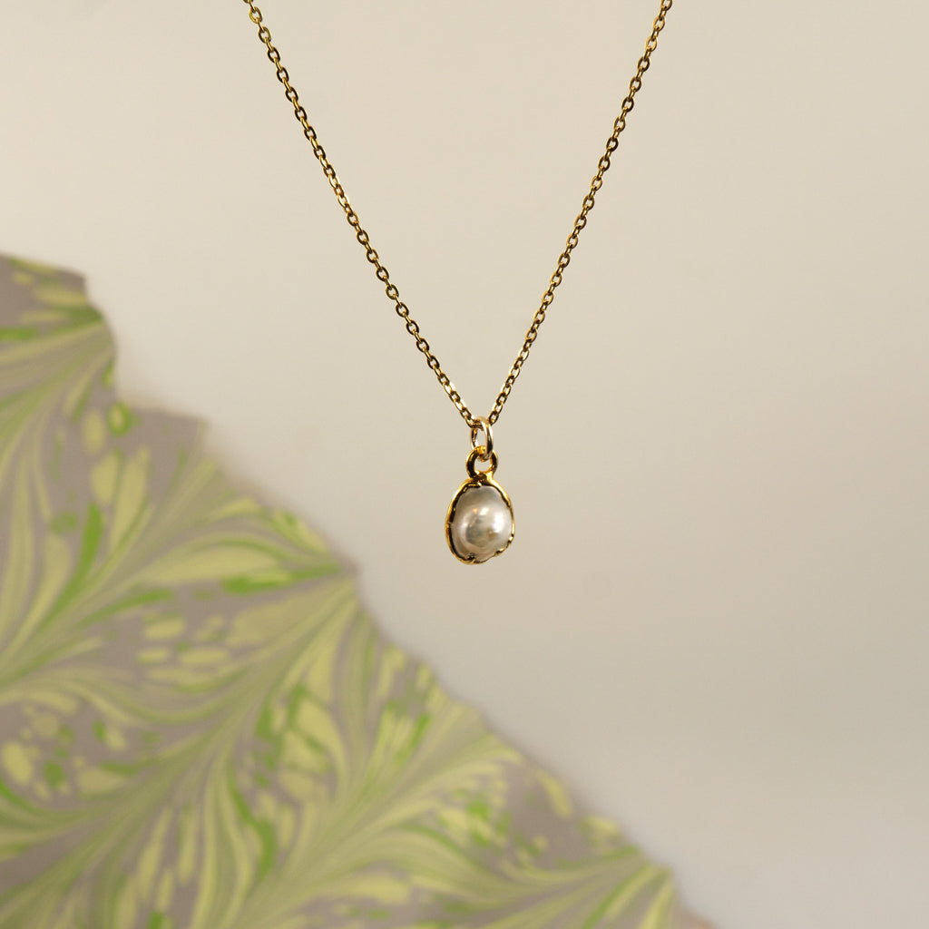 A delicate gold chain necklace with a small irregular pearl pendant, 