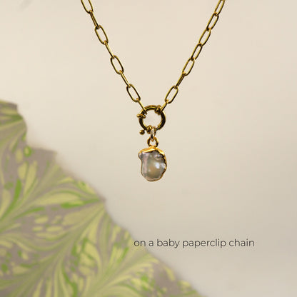 A gold paperclip chain necklace with a small gold ring clasp holding an irregular, pearl pendant, 