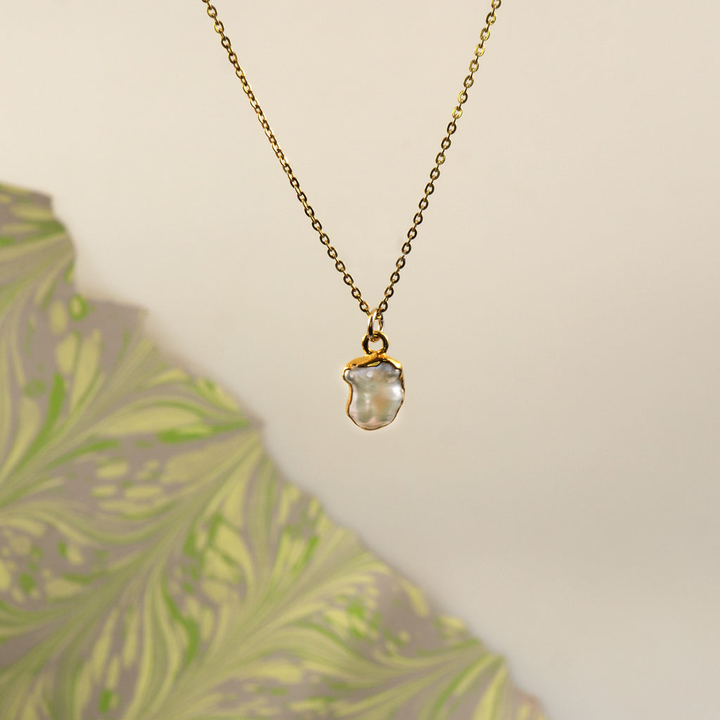 A gold chain necklace with a irregular-shaped pearl pendant,