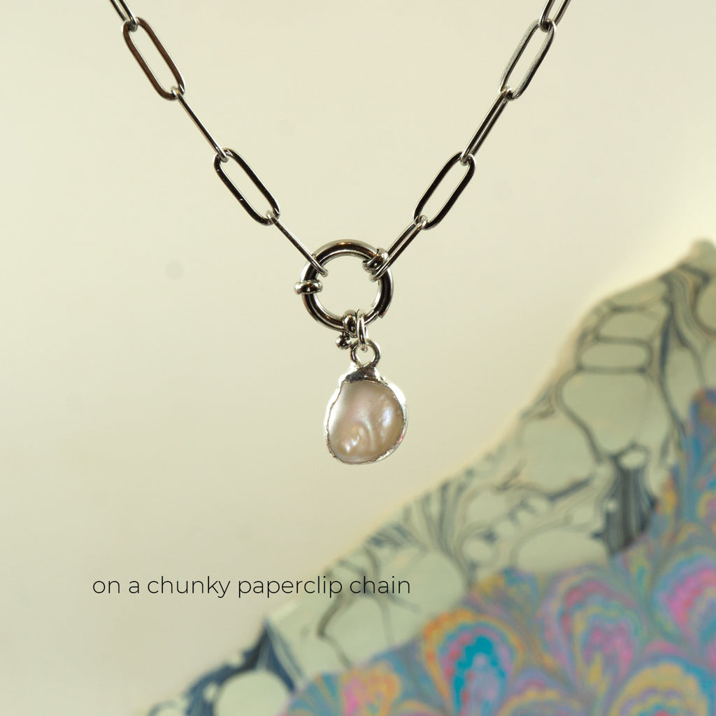 A silver paperclip chain necklace with a small ring clasp holding a baroque pearl pendant,