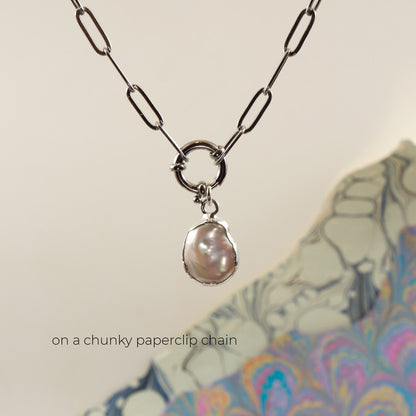 A silver paperclip chain necklace with a large ring clasp holding a single irregular baroque pearl pendant, 