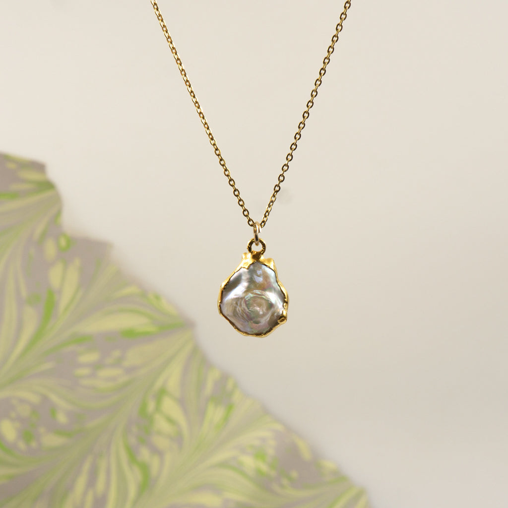 A gold chain necklace with a small gold with irregular pearl pendant