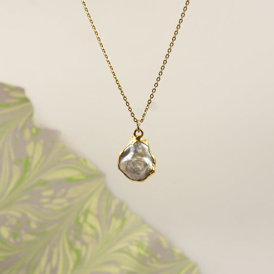 A gold chain necklace with a small gold with irregular pearl pendant