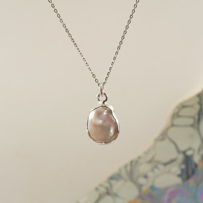 A silver chain necklace with a bezel-set baroque pearl pendant