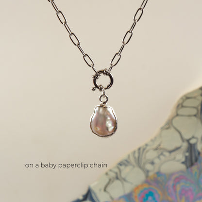 A silver paperclip chain necklace with a small ring clasp holding an irregular, pearl pendant, 