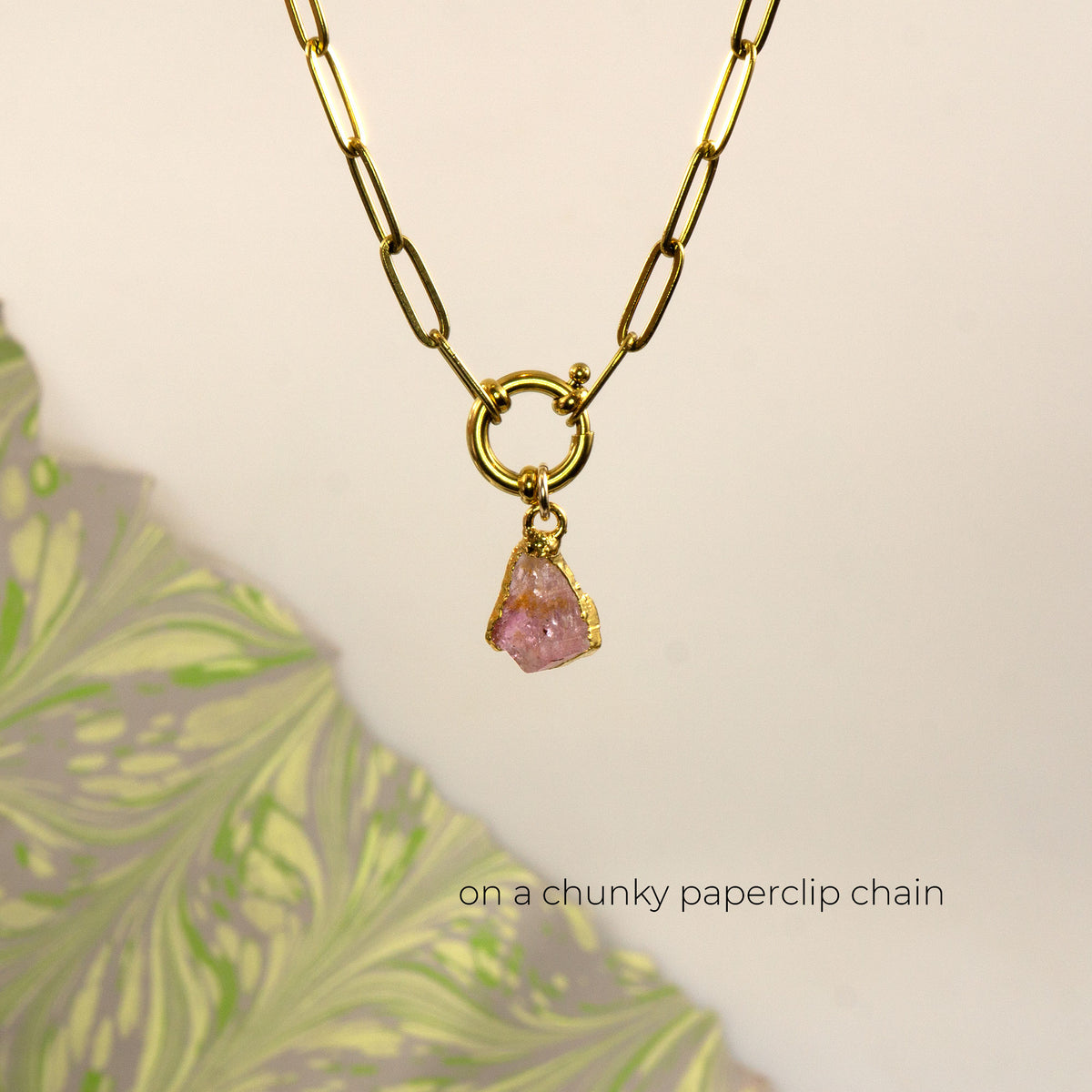 A gold paperclip chain necklace with a small gold ring clasp and a dangling raw Pink Tourmaline stone pendant