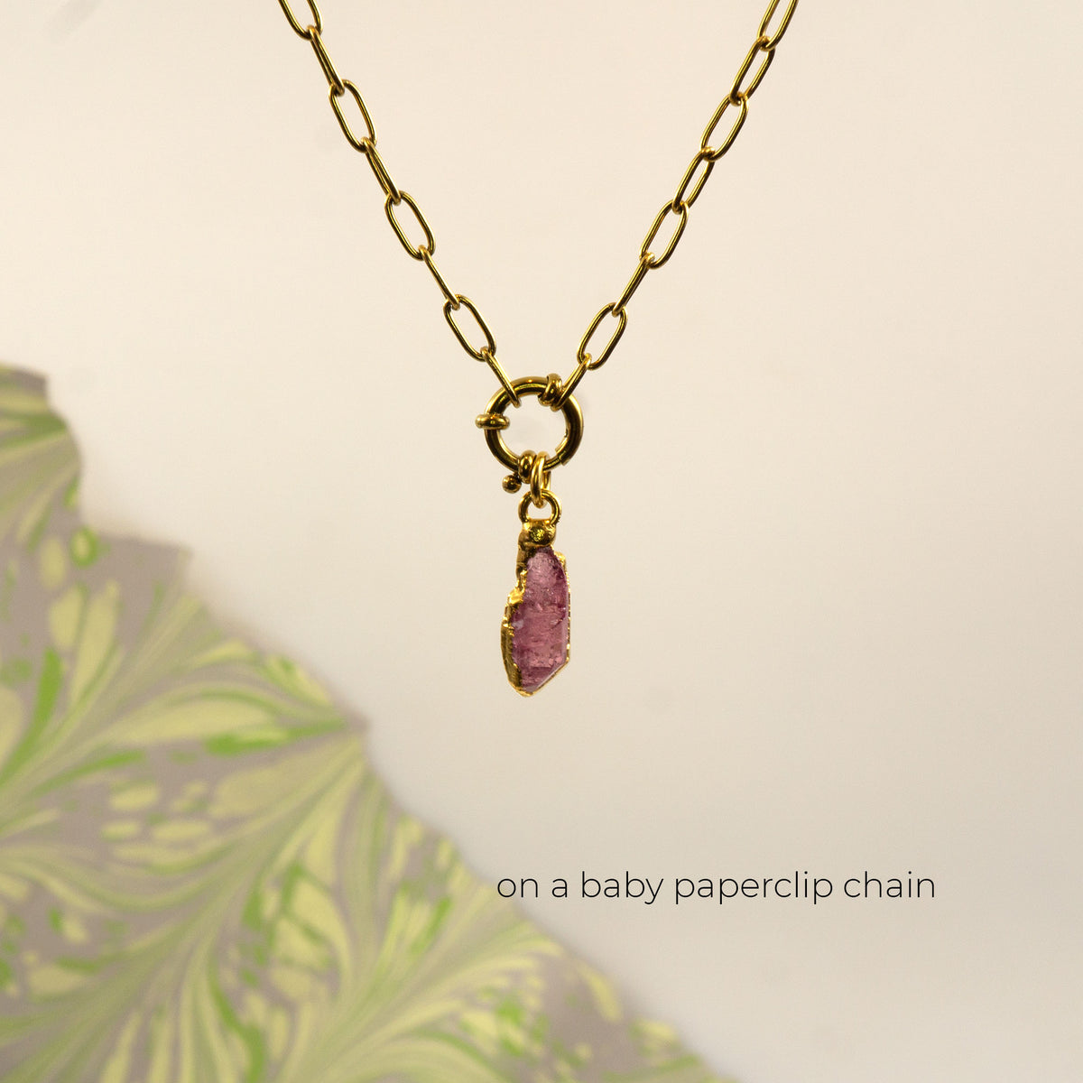 A gold paperclip chain necklace with a small gold ring clasp holding a raw Pink Tourmaline gemstone pendant