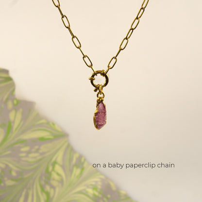 A gold paperclip chain necklace with a small gold ring clasp holding a raw Pink Tourmaline gemstone pendant