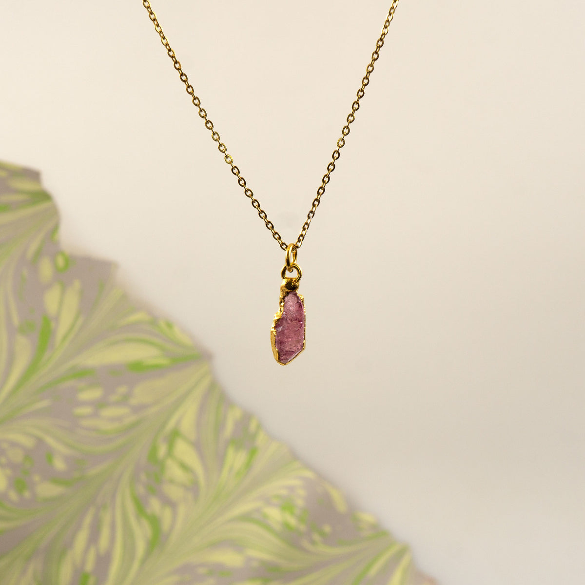 A gold chain necklace with a raw, polished pink tourmaline stone pendant.