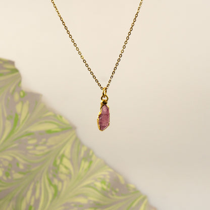 A gold chain necklace with a raw, polished pink tourmaline stone pendant.