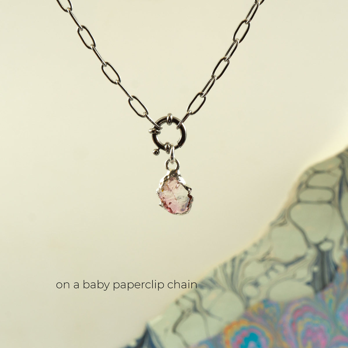 A silver paperclip chain necklace with a small ring clasp and a teardrop-shaped Pink Tourmaline gemstone pendant