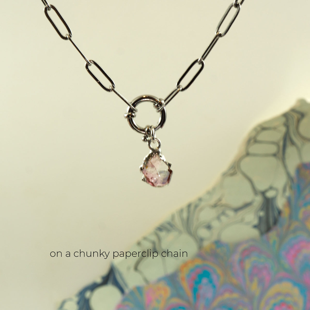 A silver paperclip chain necklace with a circular ring clasp and a small Pink Tourmaline teardrop gemstone pendant