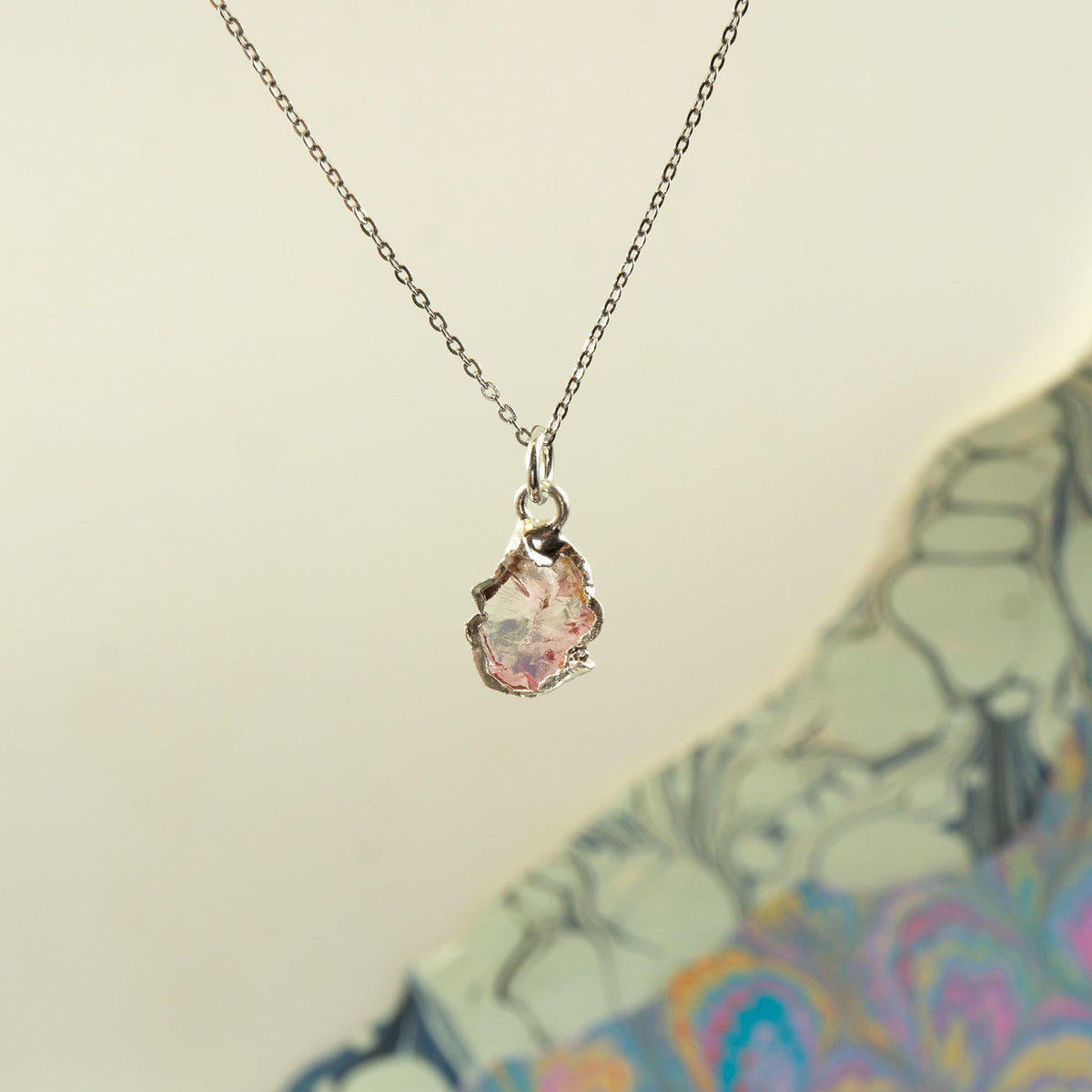 A silver chain necklace with a raw, irregular-cut Pink Tourmaline gemstone pendant