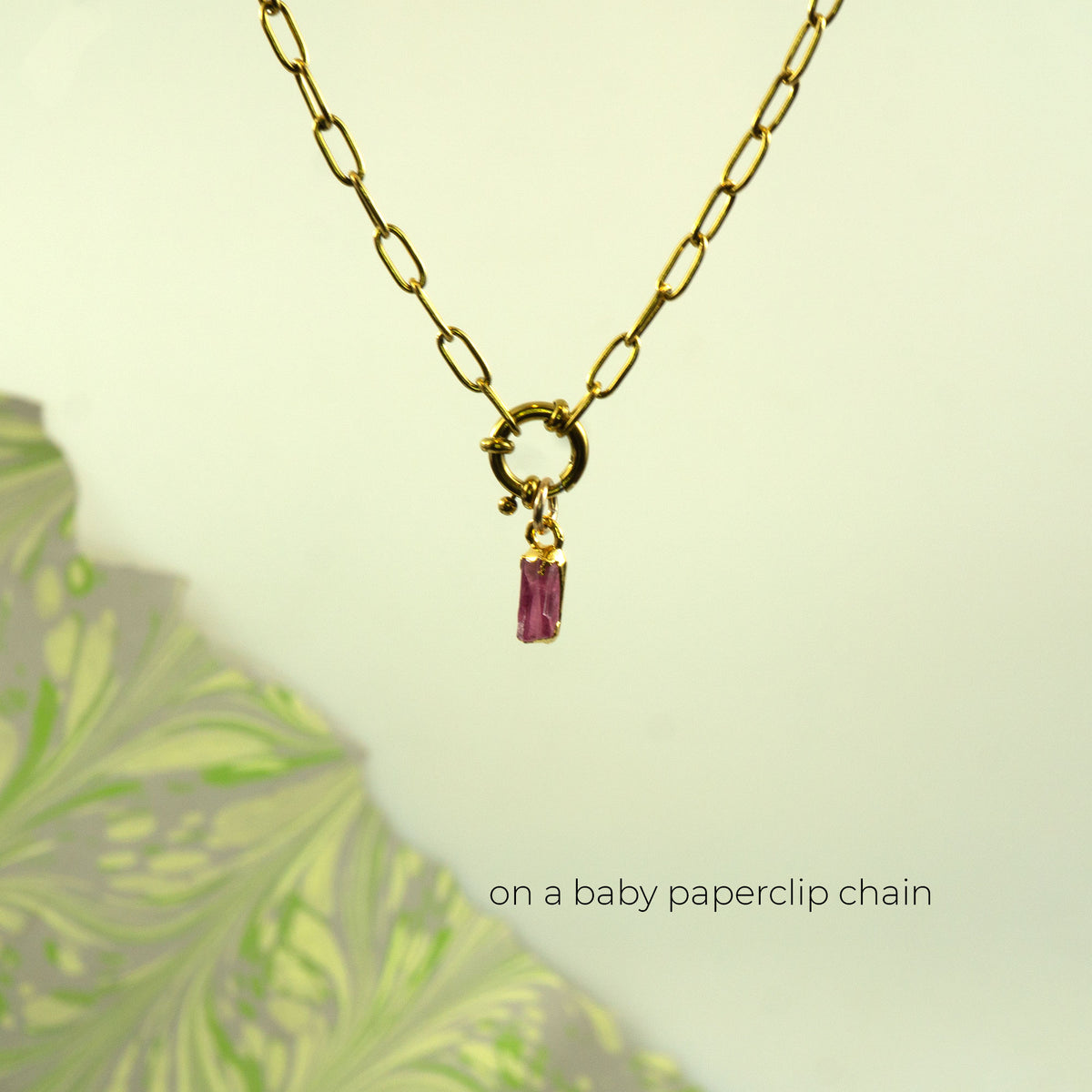 A gold paperclip chain necklace with a small gold ring clasp and a dangling Pink Tourmaline rectangular gemstone.