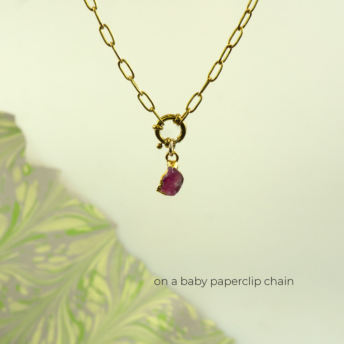 A gold paperclip chain necklace with a small gold clasp and a dangling raw Pink Tourmaline gemstone pendant