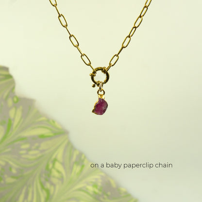 A gold paperclip chain necklace with a small gold clasp and a dangling raw Pink Tourmaline gemstone pendant