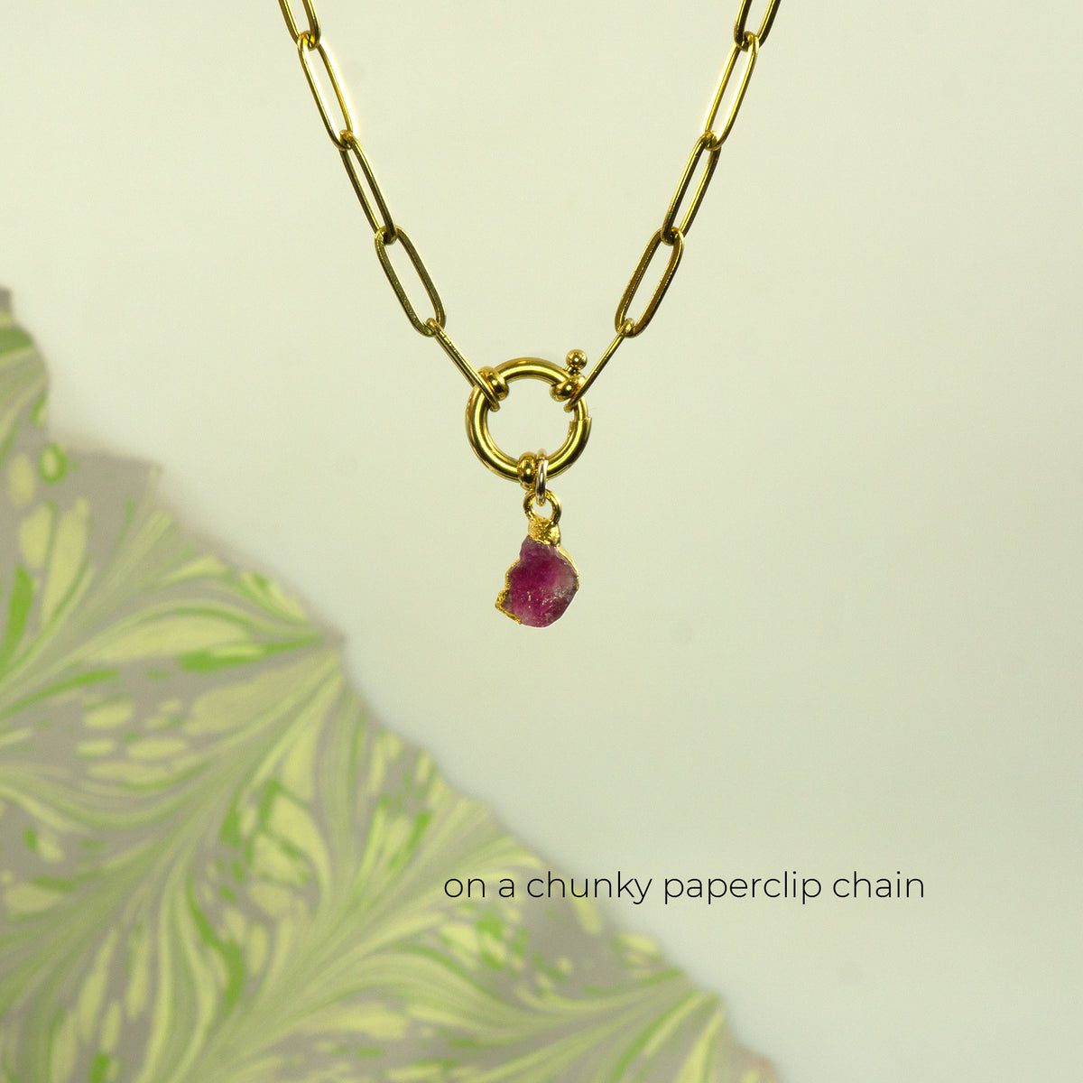A gold paperclip chain necklace with a small ring clasp and a dangling raw Pink Tourmaline gemstone
