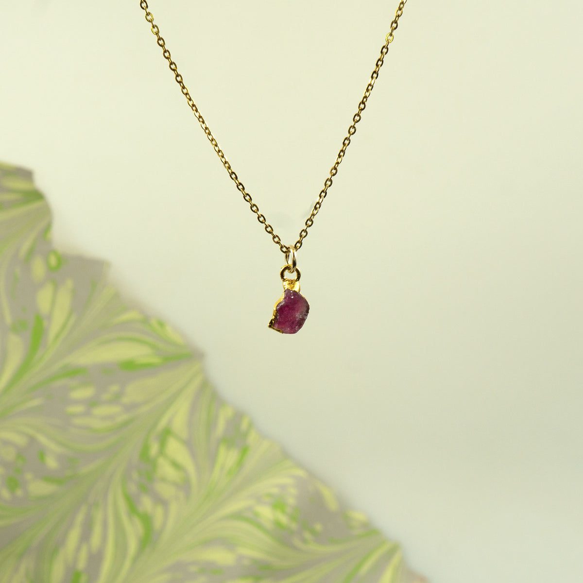 A delicate gold chain necklace with a small, rough-cut Pink Tourmaline gemstone pendant